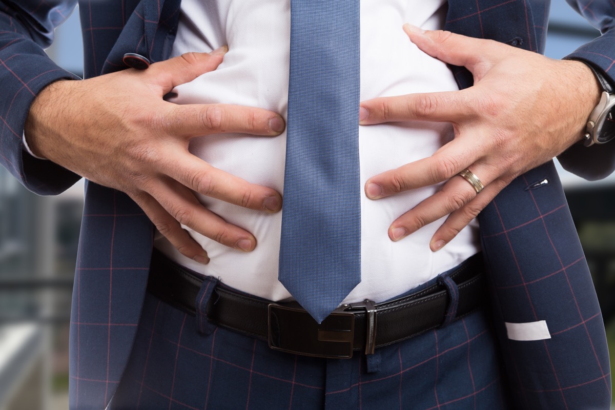 Man in a suit holding his bloated stomach