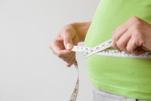 Overweight woman measuring her waist.