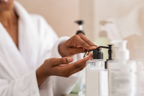 woman hands using cosmetic liquid soap in bathroom. Close up hands in bath robe using body lotion dispenser after shower