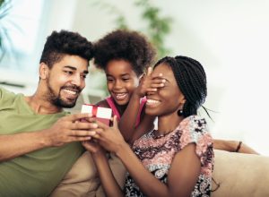 black mother, father, and daughter opening present on couch