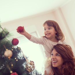 hispanic woman with daughter on her shoulders decorating a christmas tree