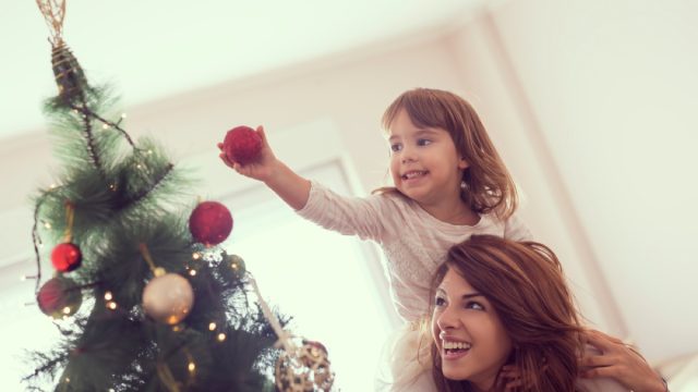 hispanic woman with daughter on her shoulders decorating a christmas tree