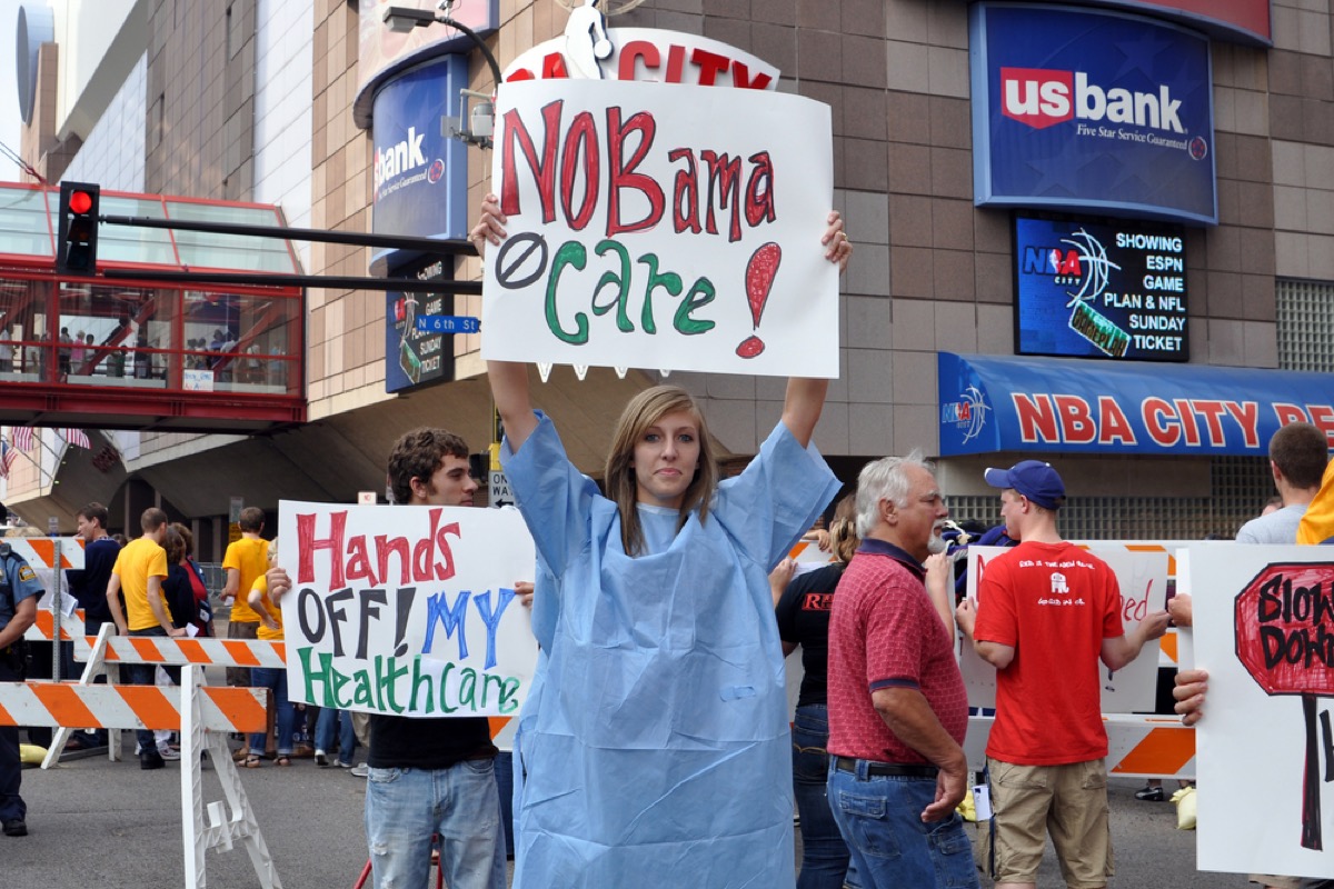 Young woman in hospital gown holds up "Nobama Care" sign in Minneapolis in 2009