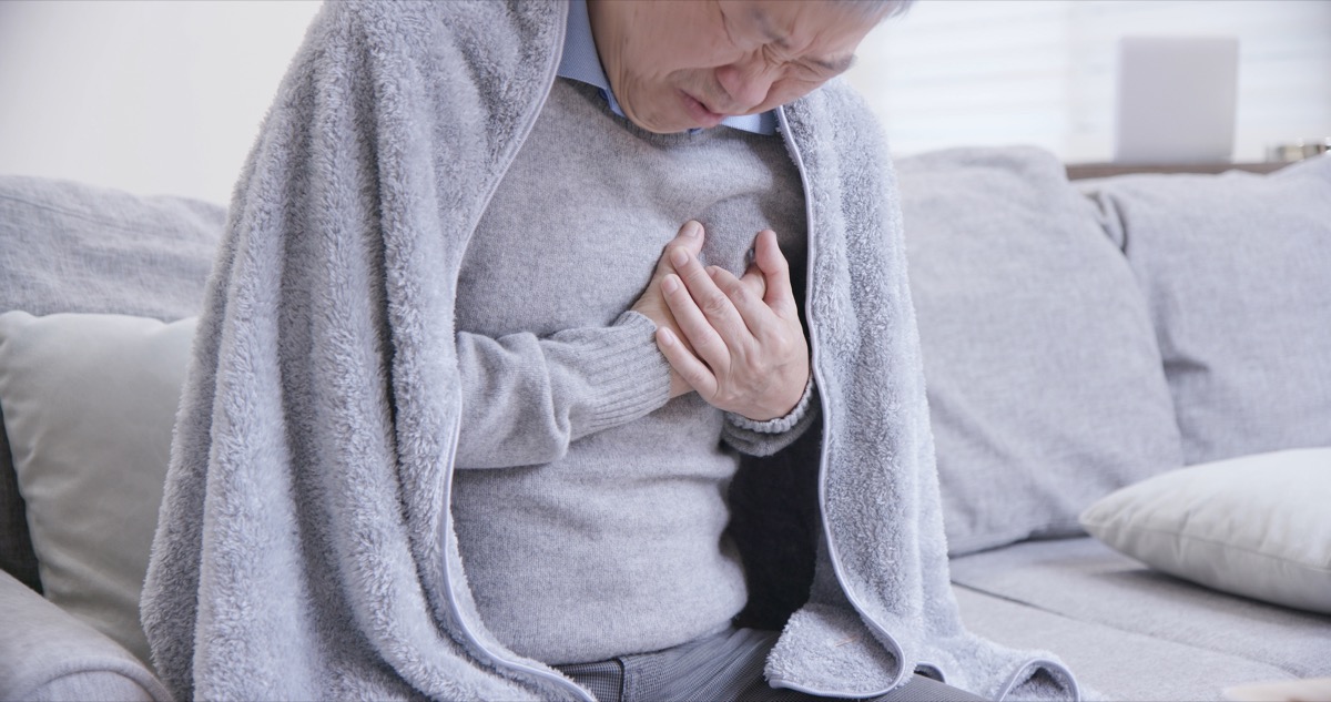 Man sitting on the couch with a blanket holding his chest in pain