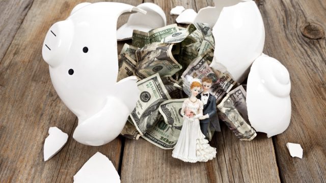 A broken piggy bank with crumpled bills and a wedding cake couple.