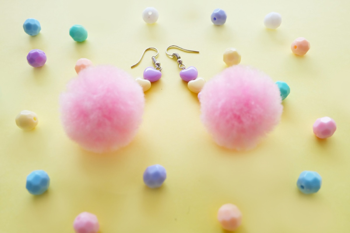 pink pom pom earrings on yellow background with pastel colored heart beads