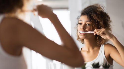 young woman brushing her teeth in the mirror