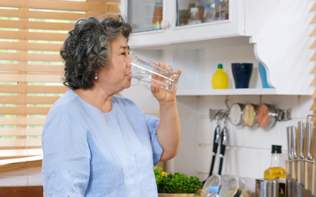Older Asian woman drinking water in the kitchen