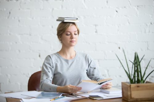 Portrait of attractive woman at desk, books on her head