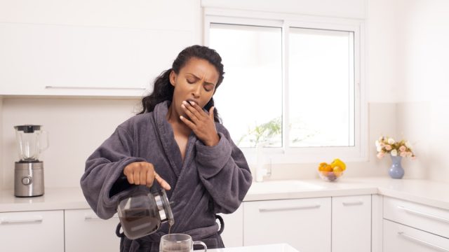 Woman yawning while she pours herself some coffee