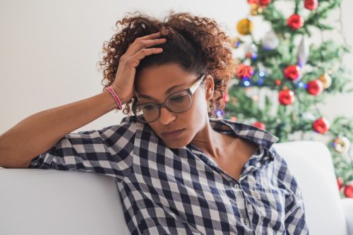 Woman looking upset and sad next to a Christmas tree