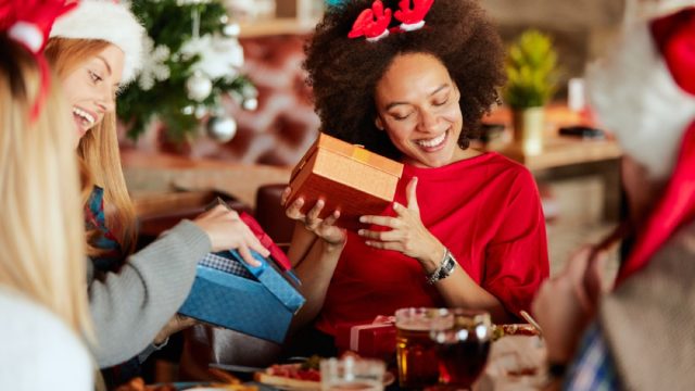 young black woman opening gifts sitting next to blonde friend holding box