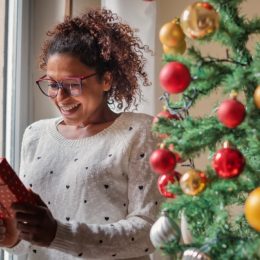 young black woman holding gift in front of christmas tree