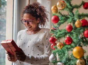 young black woman holding gift in front of christmas tree