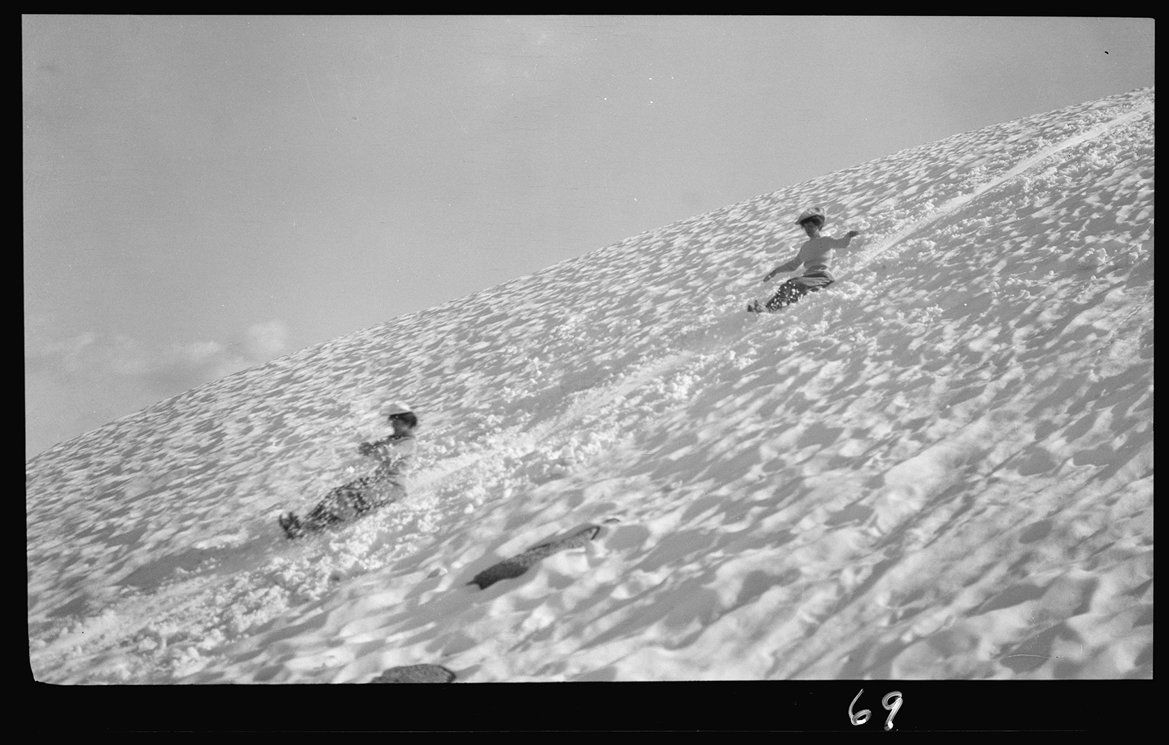 two women sled down a snowy hill