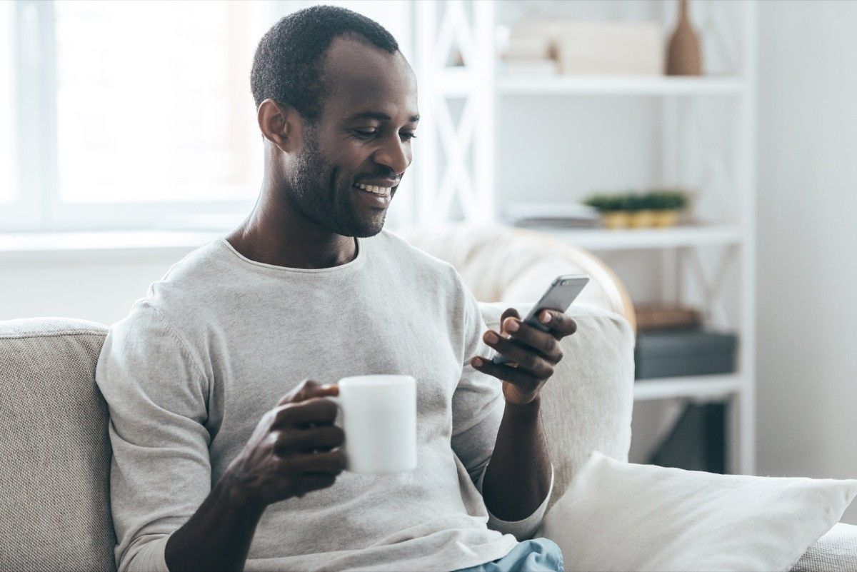 middle aged man texting on couch with cup of tea