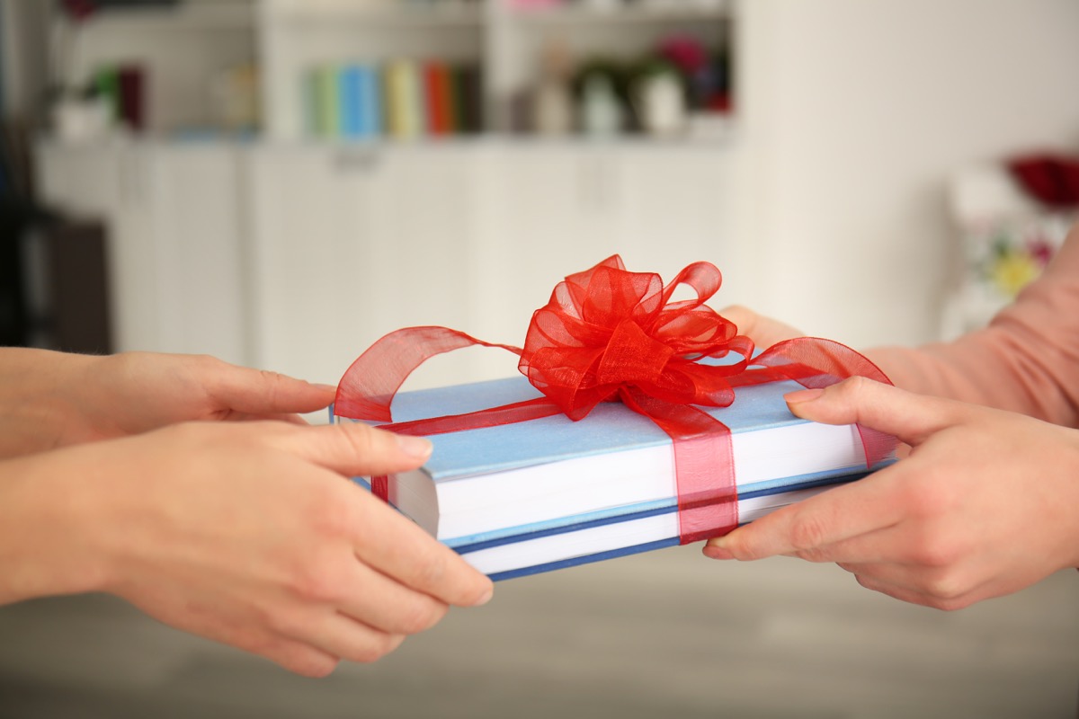 Person giving a book as a holiday gift with a ribbon on it