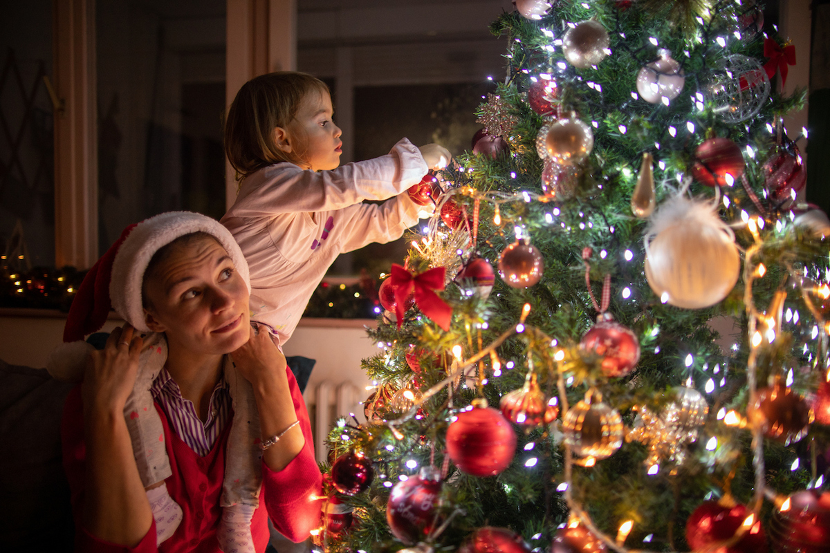 Mother carrying her daughter on shoulder while decorating the Christmas tree