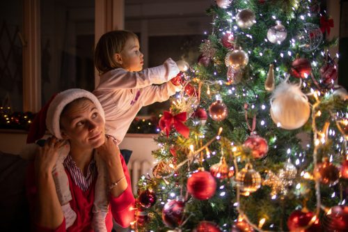 Mother carrying her daughter on shoulder while decorating the Christmas tree