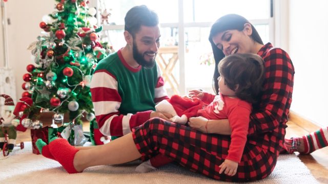 hispanic mother, father, and daughter wearing christmas pajamas in front of christmas tree