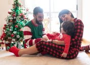 hispanic mother, father, and daughter wearing christmas pajamas in front of christmas tree