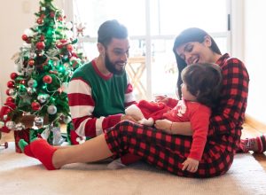 hispanic mother, father, and daughter wearing christmas pajamas in front of christmas tree