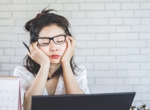 young asian woman falling asleep at her desk