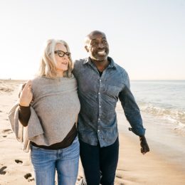 older couple walking on the beach with their arms around each other