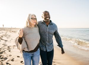 older couple walking on the beach with their arms around each other