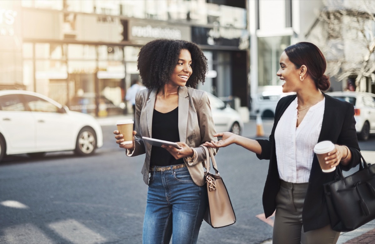 black businesswoman and latina businesswoman chatting with coffee on the street