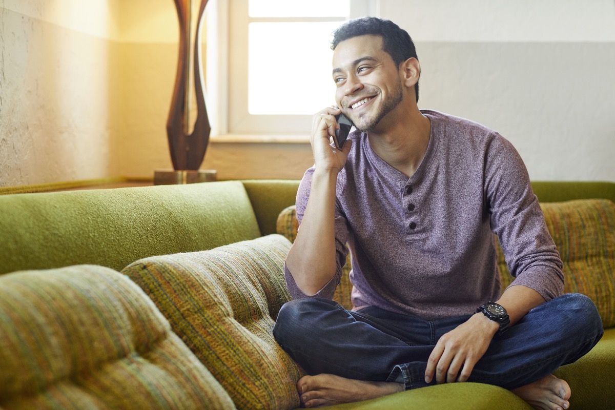 young man happily chatting on the phone on the couch
