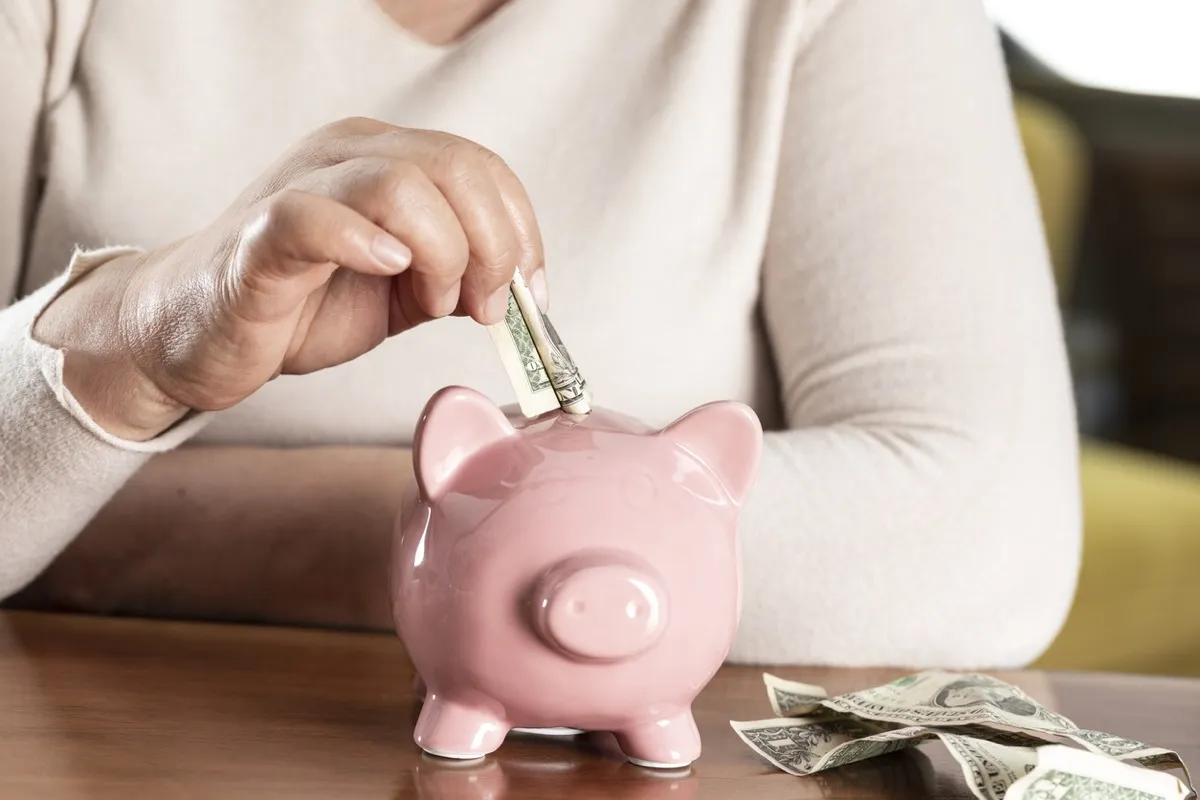 close up of older white woman putting money in a piggy bank