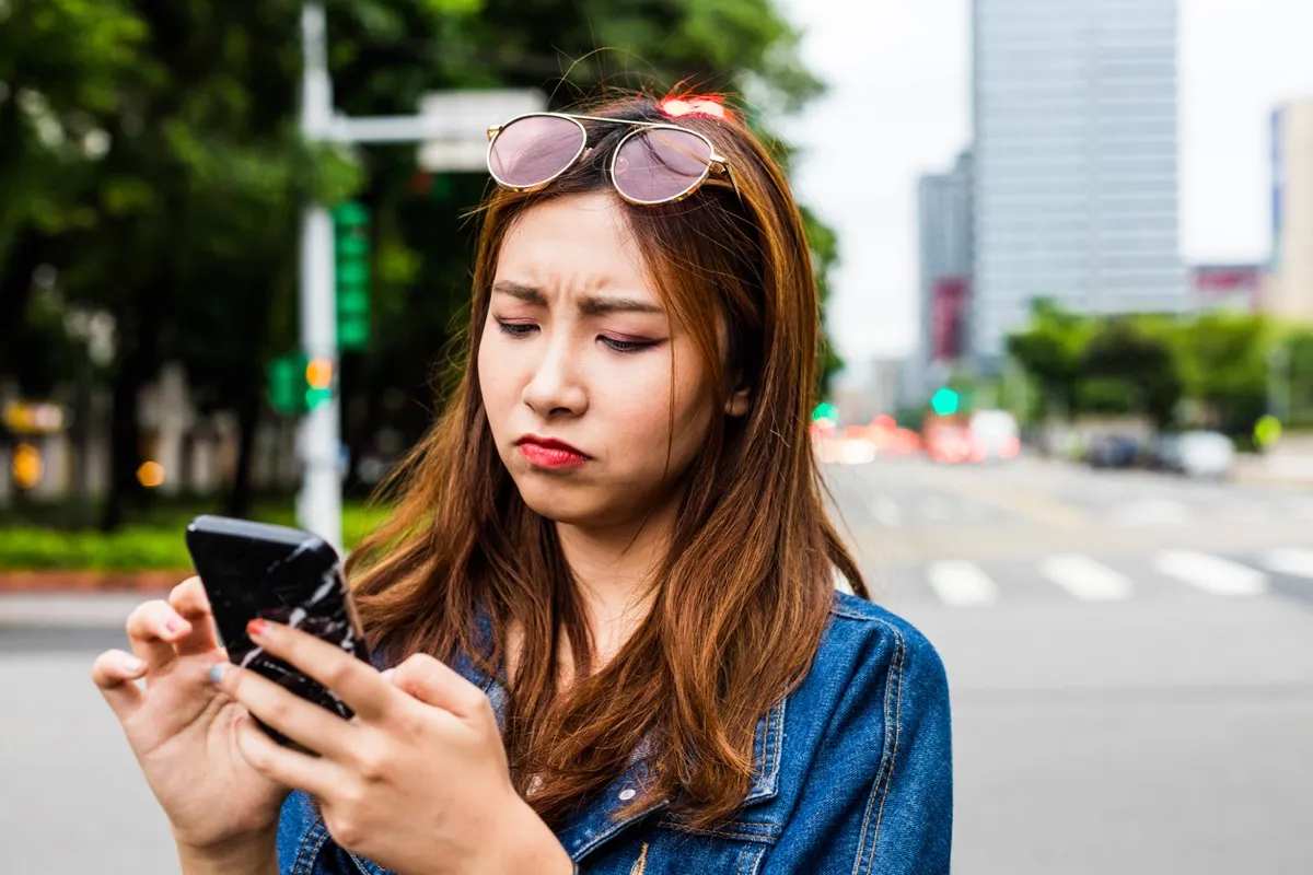 young asian woman looking disappointed while she uses her phone on the street