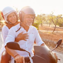 older couple riding a motor scooter on a country road