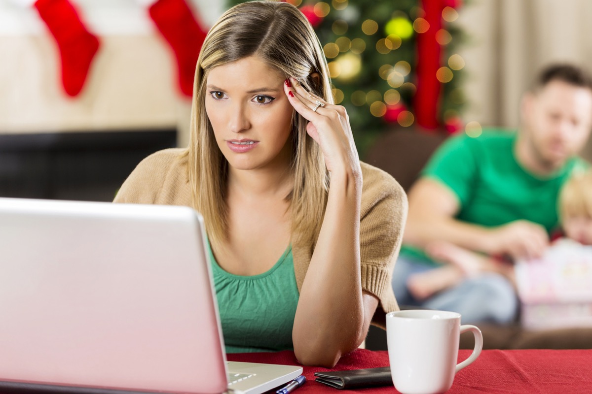 white woman looking anxiously at computer with family in the background on christmas