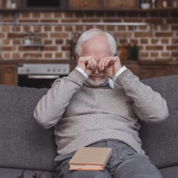 older man rubbing his eyes on the couch