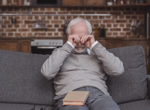 older man rubbing his eyes on the couch