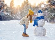 little girl outside in winter with snowman