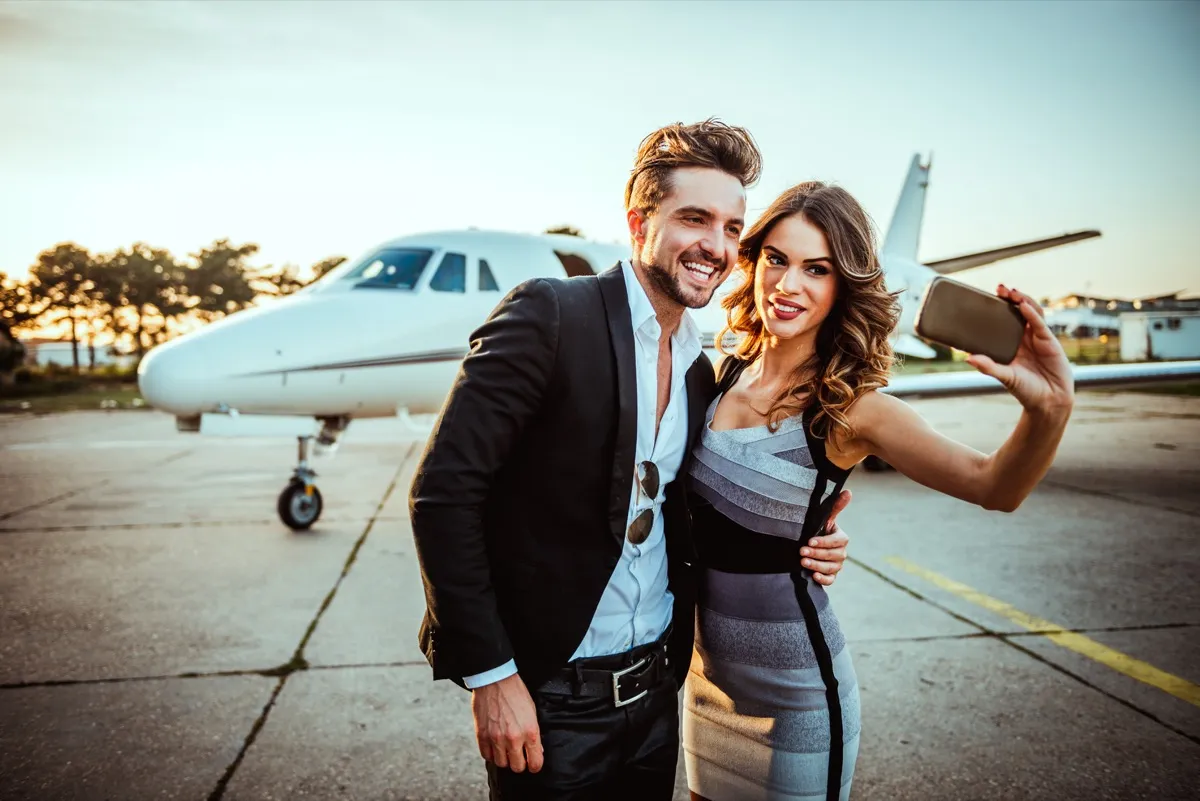 rich and famous couple taking selfie in front of private jet