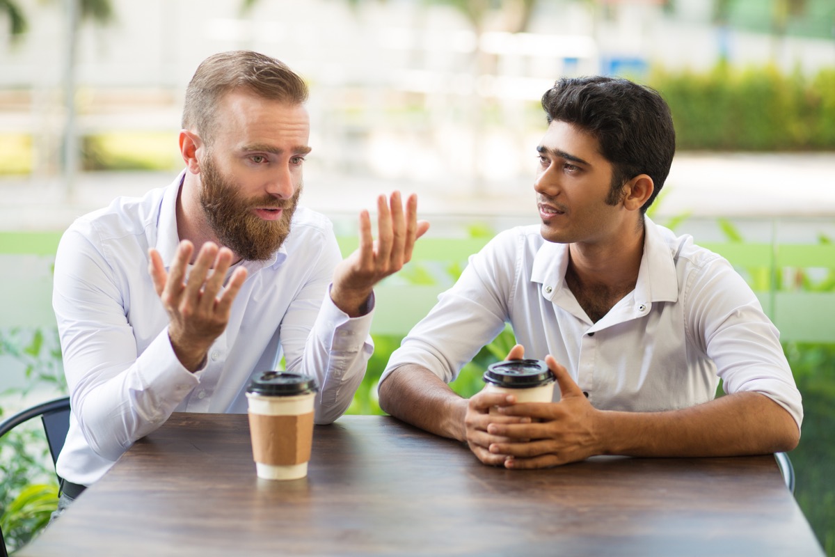 man apologizing to his friend talking while getting a cup of coffee