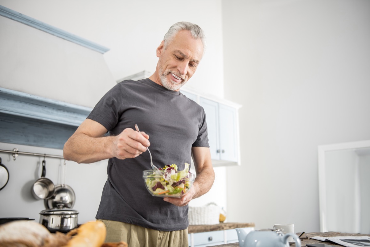 Older man eating a healthy salad in the kitchen