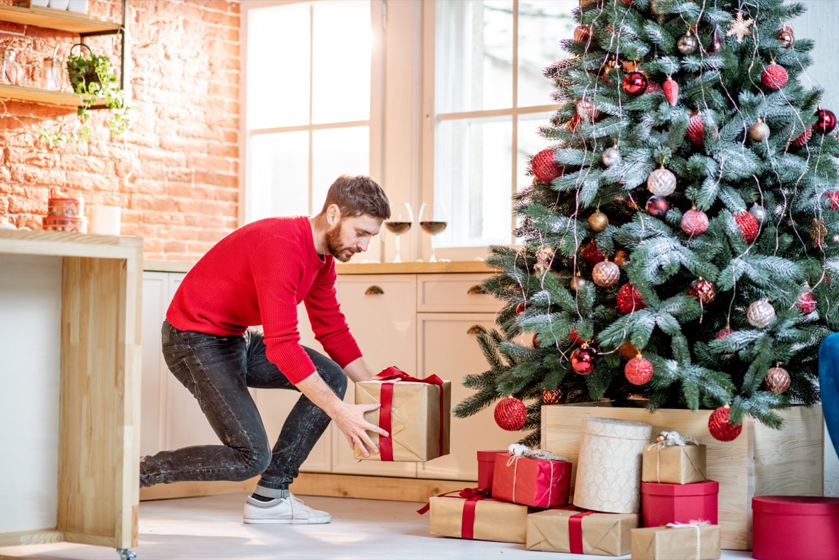 Man putting gifts under the Christmas tree preparing for a New Year holidays at home