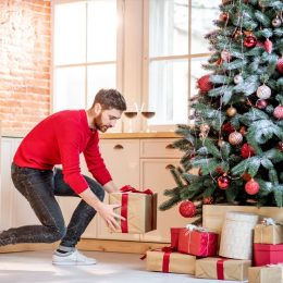 Man putting gifts under the Christmas tree preparing for a New Year holidays at home