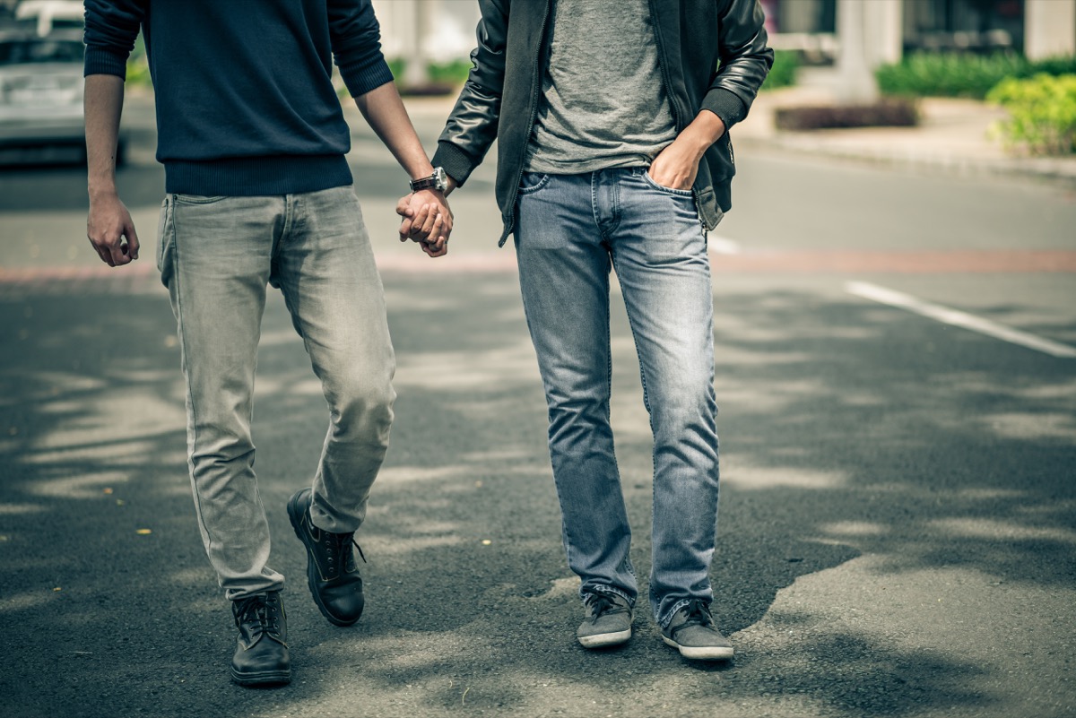 two men in jeans holding hands outdoors