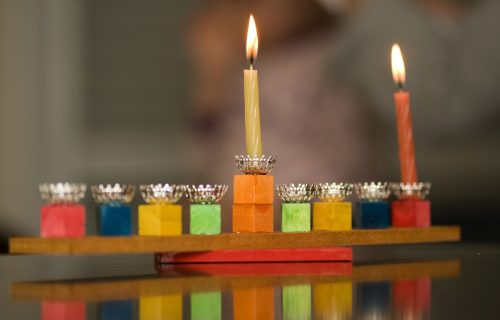 wooden menorah with lit shamash and first night candle