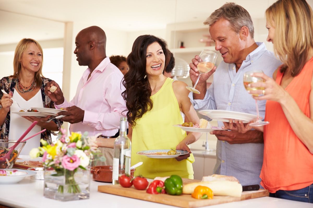 middle aged people drinking wine in kitchen at party