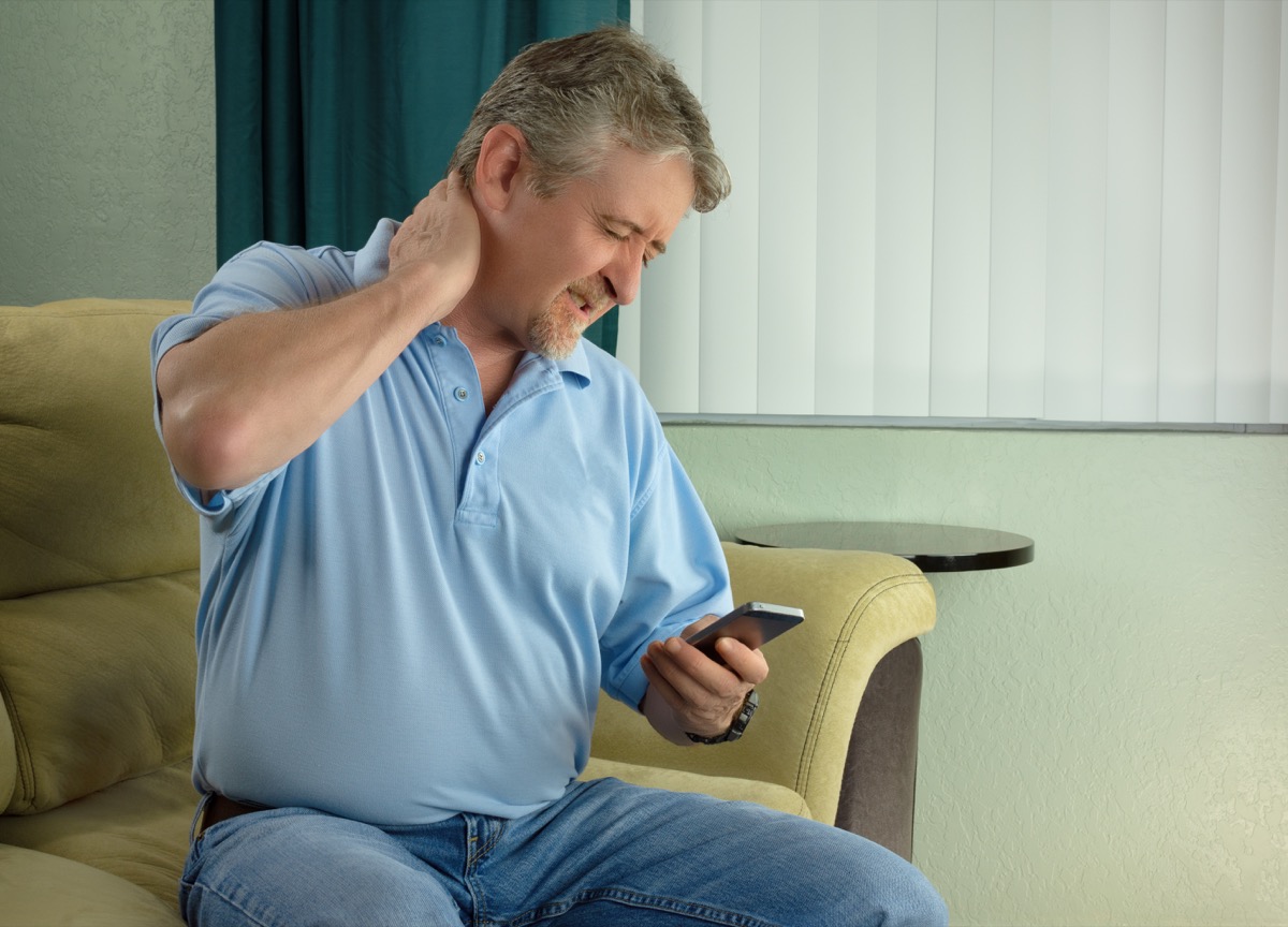 Man looking at his phone and rubbing his neck in pain