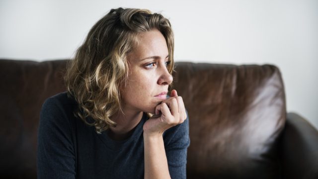 nervous woman staring out of the window while sitting on a brown couch
