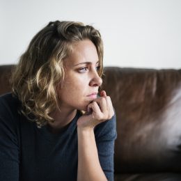 nervous woman staring out of the window while sitting on a brown couch