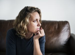 nervous woman staring out of the window while sitting on a brown couch